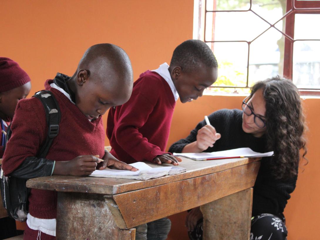 A young child gets academic help from a volunteer during her teaching project in Tanzania. A volunteer teaching abroad, helps children with their classwork in Tanzania.